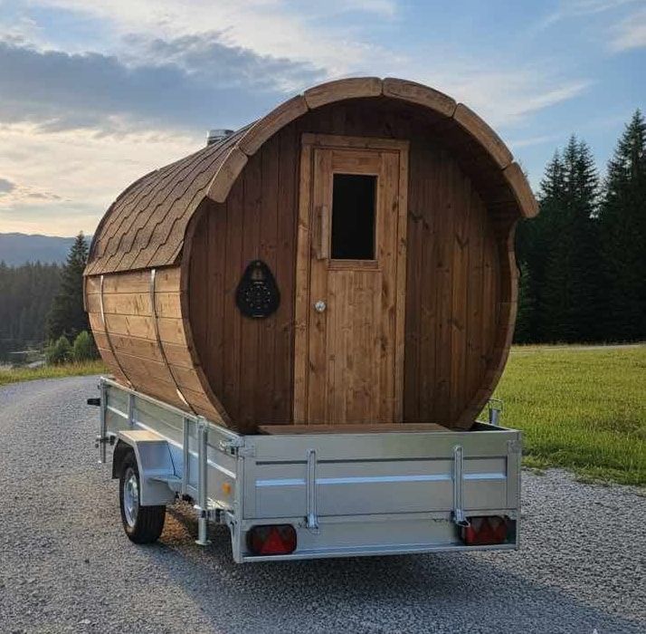 Wooden barrel sauna on a trailer by a lake, with a code key box beside the door
