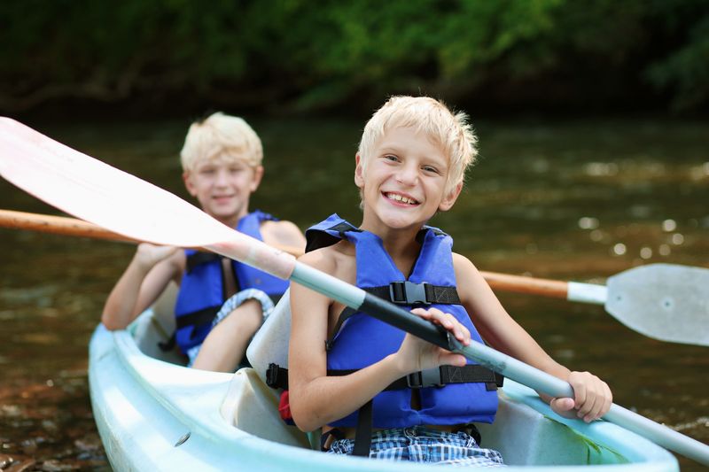 Two smiling boys in life jackets paddling a kayak