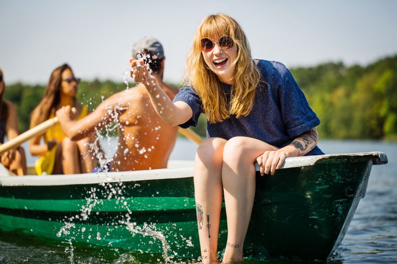 Laughing friends splashing water from a green boat on a lake