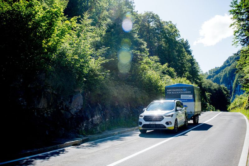 Car towing a trailer along a winding forest road