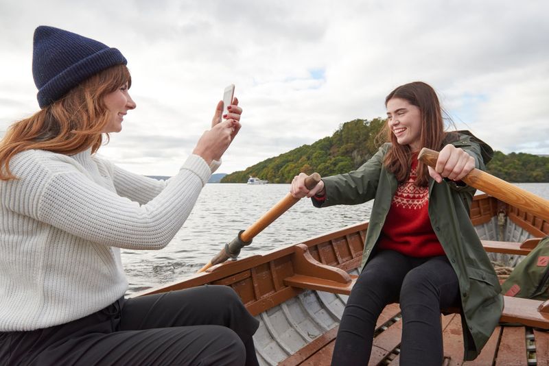 Two friends in a wooden rowing boat – one rowing and one taking a photo