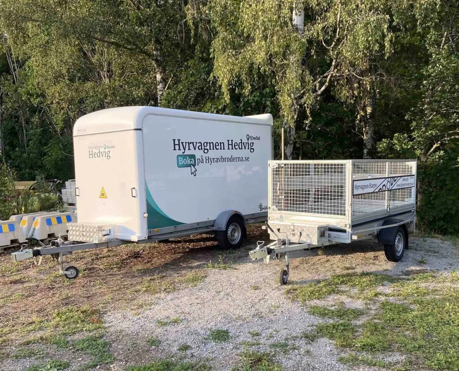 Two trailers from Hyr Av Bröderna, box trailer Hyrvagnen Hedvig and mesh trailer Hyrvagnen Harpo, parked and ready for self-service rental.
