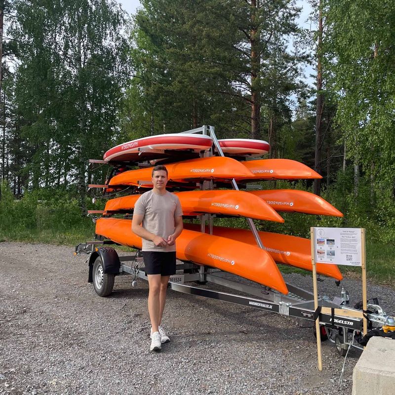 Kajup's self-service kayak trailer loaded with orange kayaks at the water's edge
