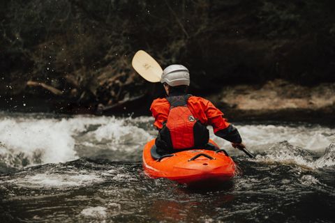 Kayaker in an orange jacket and helmet paddling down a river