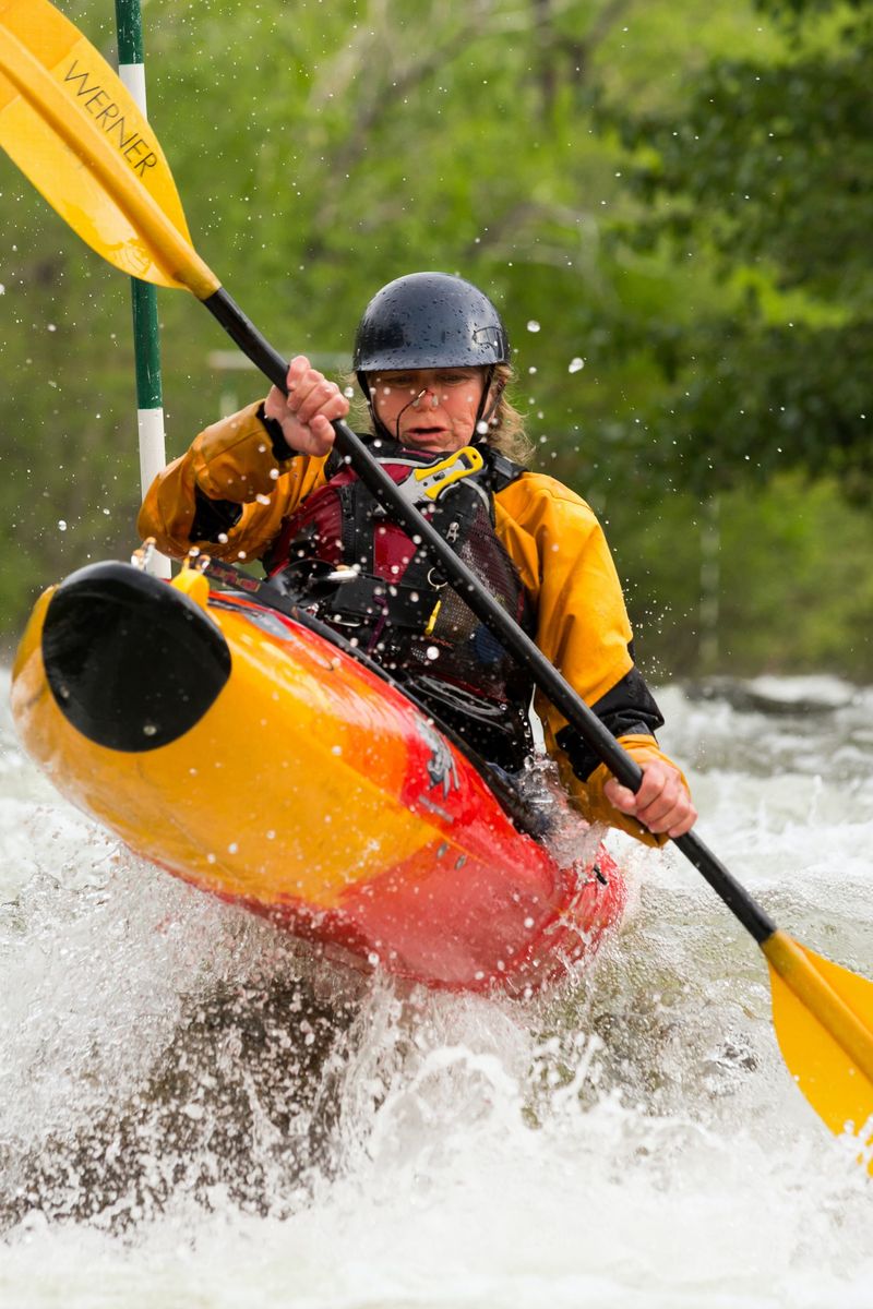 Kayaker in a helmet and yellow jacket paddling through white water