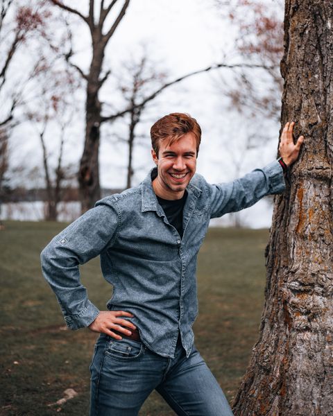 Smiling man leaning against a tree outdoors