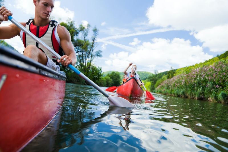 Man paddling a red canoe on a river with another canoe behind him