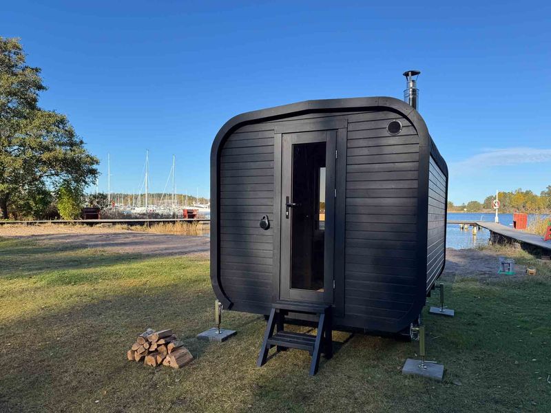 Black mobile sauna on the grass by a marina