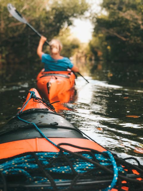 Paddlers in orange kayaks on a tree-lined river