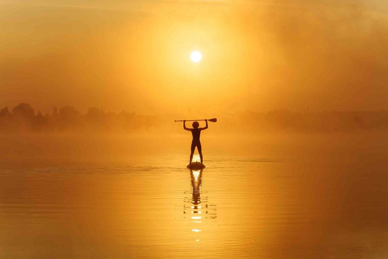 Stand-up paddleboarder on calm water at sunrise