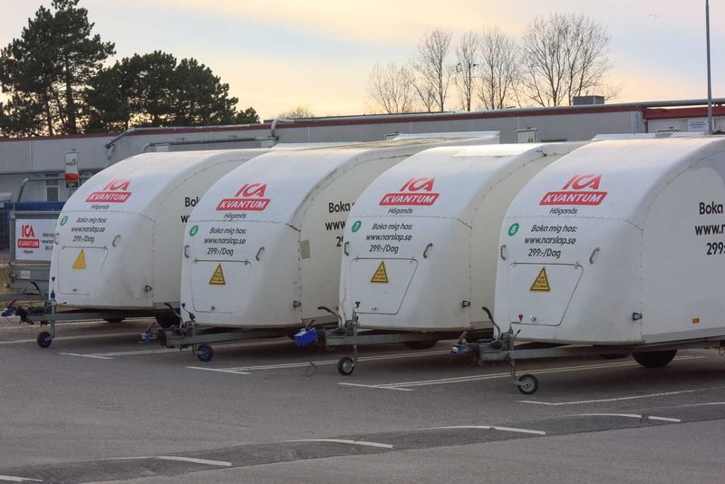 A row of enclosed rental trailers parked outside an ICA store