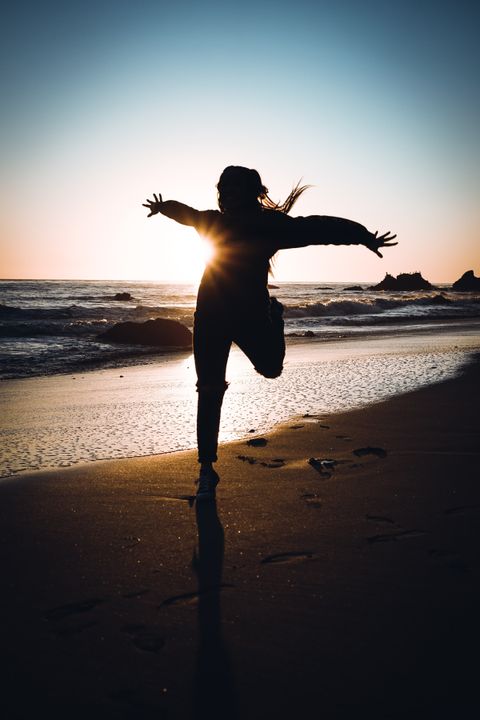 Silhouette of a person with arms raised on a beach at sunset