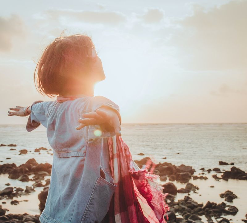 Woman enjoying the sunset by the sea with her arms outstretched