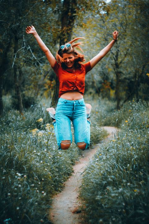 Woman jumping for joy on a path through green trees and grass